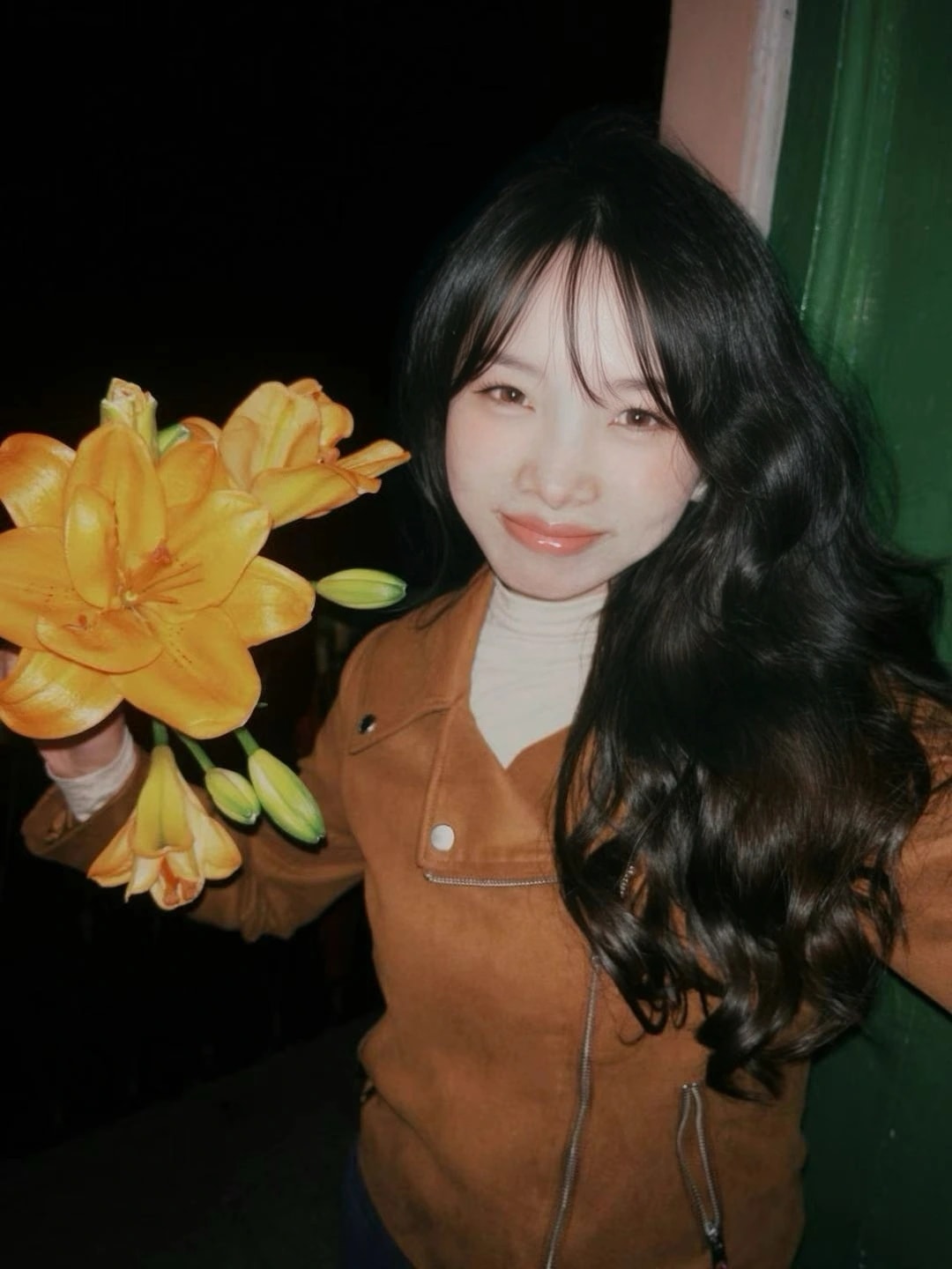 Ida holding orange flowers, standing beside a green doorway.