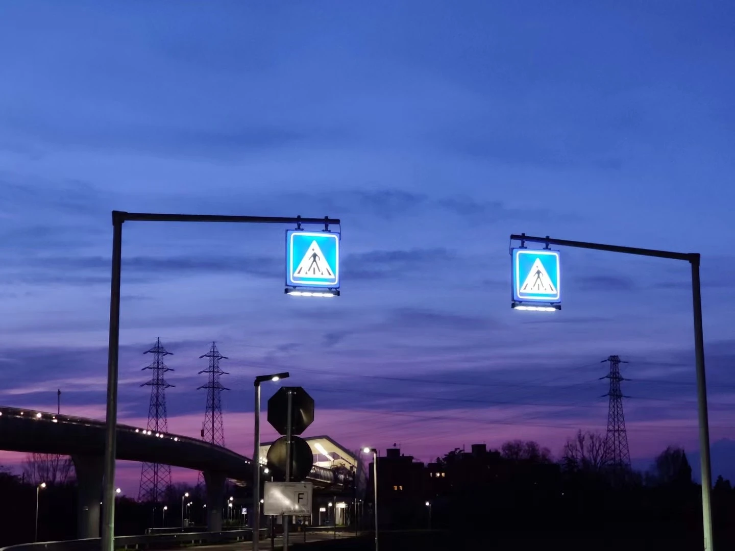 Two illuminated crossing signs under a violet evening sky