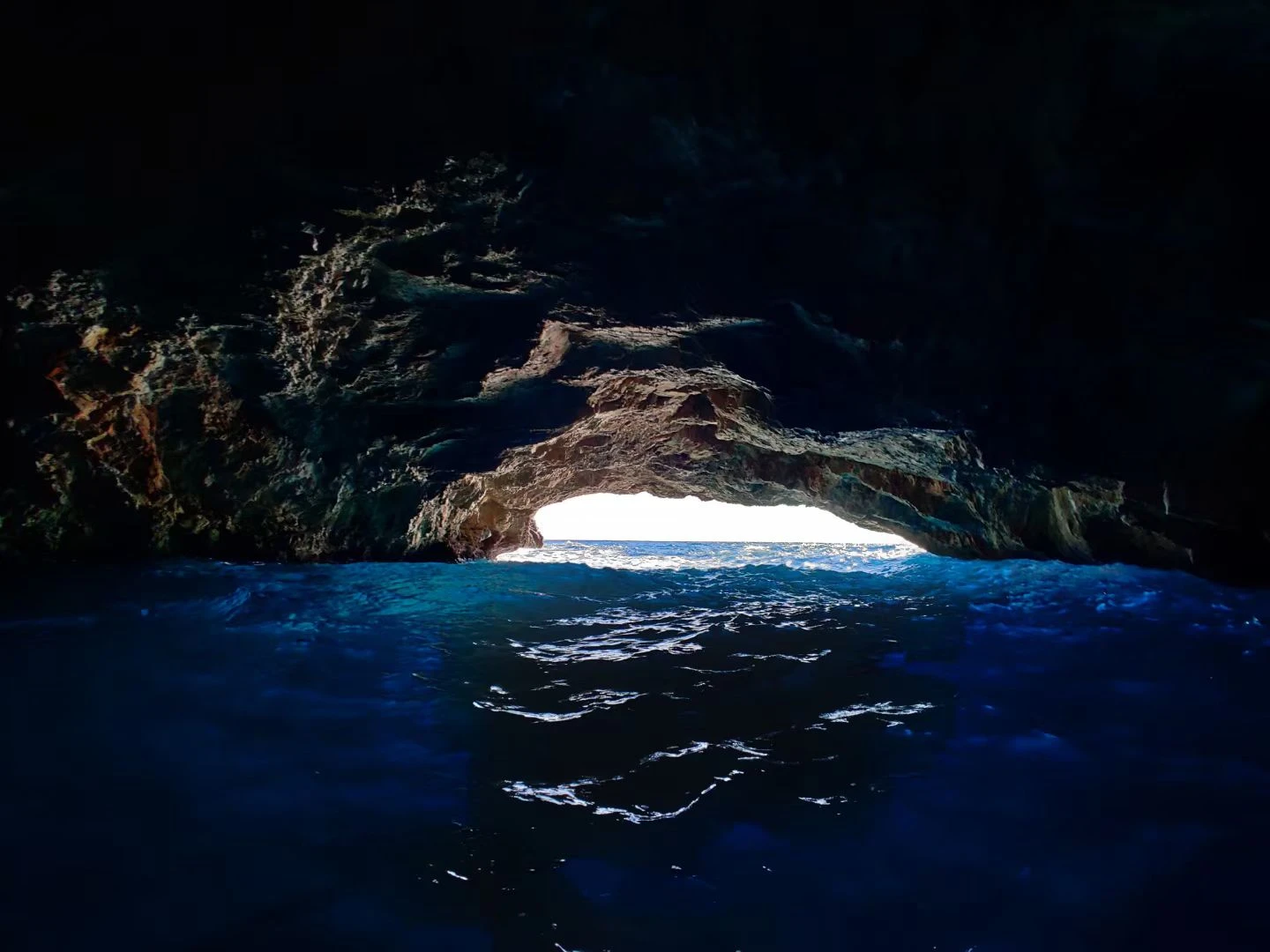 Blue water inside a dark cave with a bright opening